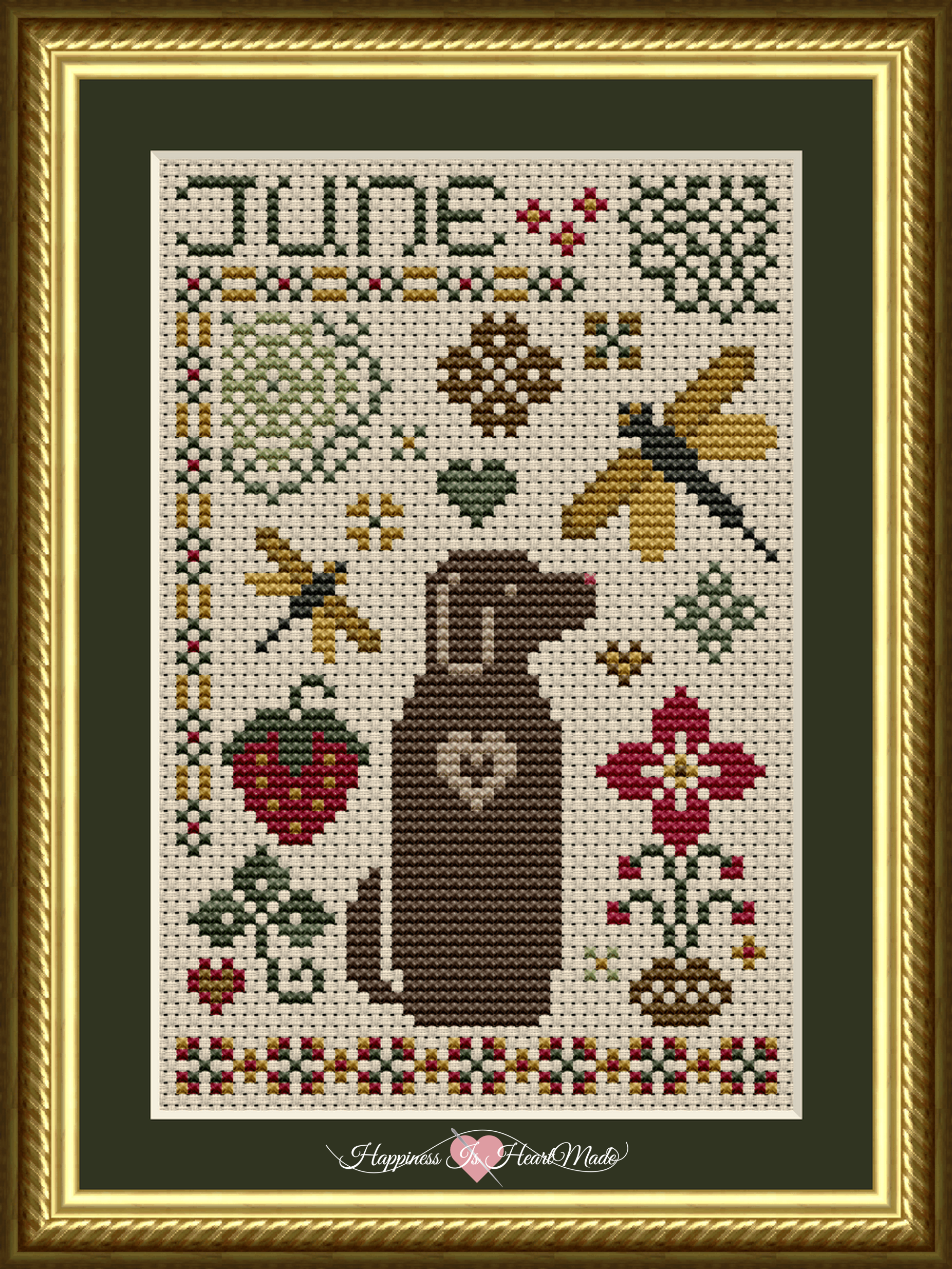 June Dog cross stitch pattern on rustic 14 count aida, in a gold colored frame. Dragonflies, flowers, and a red strawberry surround Dog in the June monthly design.